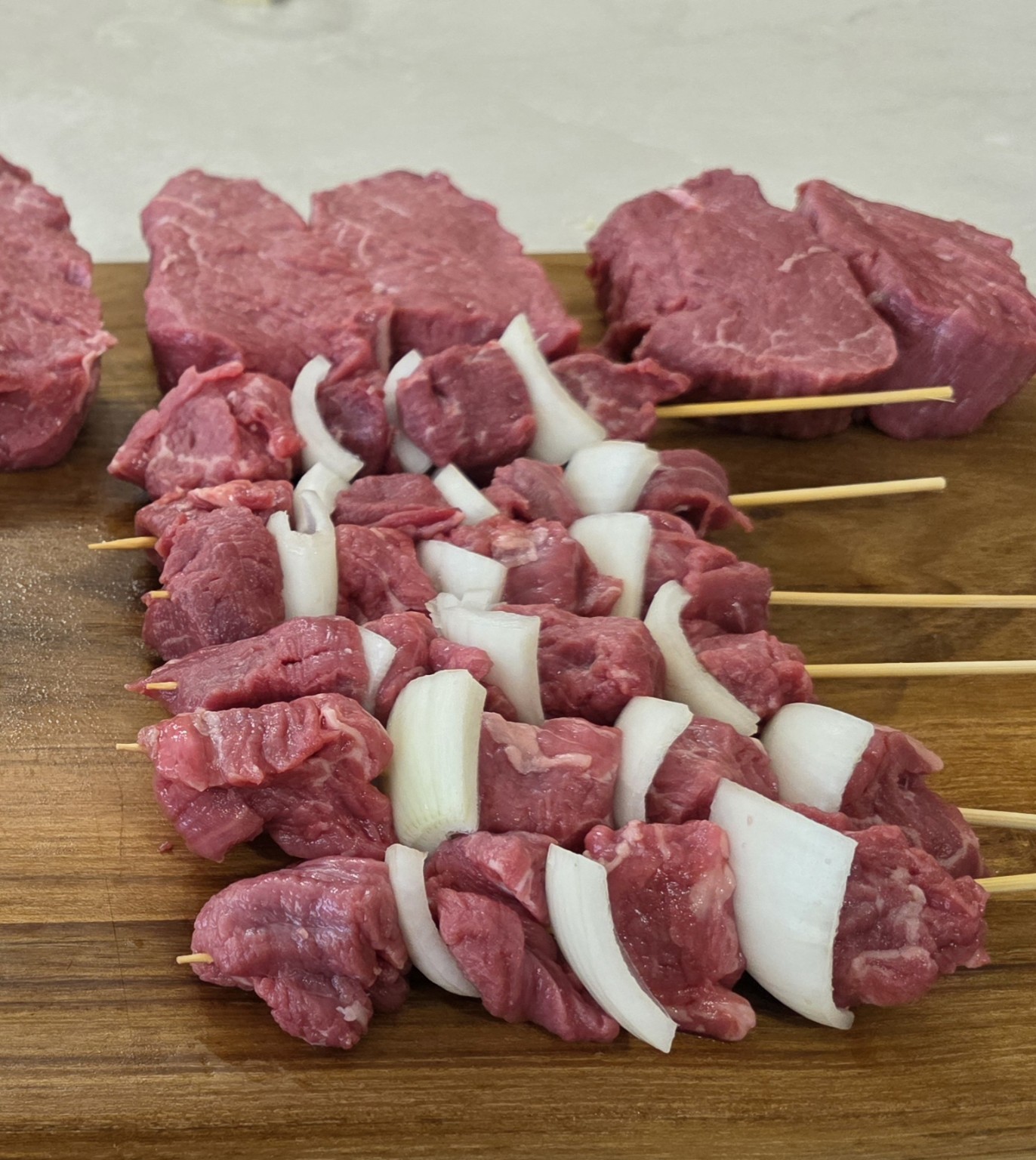 Prepared cube roll beef skewers arranged on a wooden board